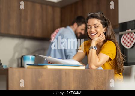 Une femme joyeuse profite d'un moment de détente à la maison, tandis que son partenaire est occupé à cuisiner en arrière-plan, créant une atmosphère chaleureuse et intime en t Banque D'Images