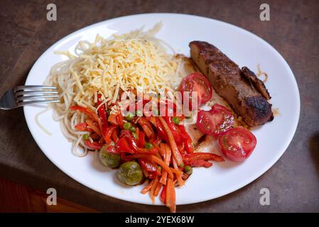 Gros plan d'un délicieux repas servi sur une assiette blanche. Le plat comprend une portion de spaghetti garnie de fromage râpé, un mélange coloré de SAU Banque D'Images