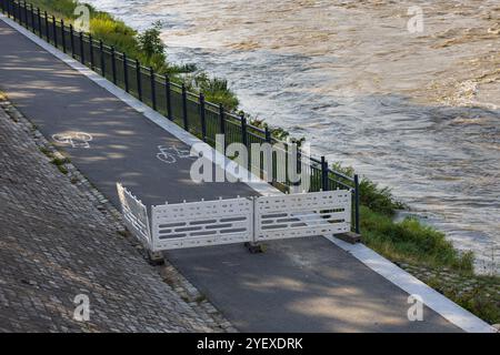 Fermeture temporaire de la piste cyclable au bord de la rivière avec des barrières de sécurité en raison de la montée des eaux lors de fortes précipitations Banque D'Images