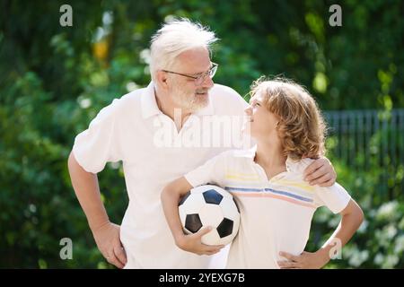 Grand-père et enfants dans le jardin ensoleillé. Famille heureuse jouant au football dans le parc d'été. Grand-père et les enfants jouent au football. Génération amour. Senior actif Banque D'Images