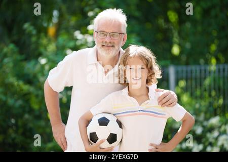 Grand-père et enfants dans le jardin ensoleillé. Famille heureuse jouant au football dans le parc d'été. Grand-père et les enfants jouent au football. Génération amour. Senior actif Banque D'Images