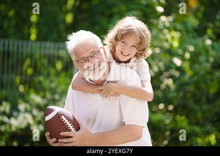 Grand-père et enfants dans le jardin ensoleillé. Famille heureuse jouant au football dans le parc d'été. Grand-père et les enfants jouent au football. Génération amour. Senior actif Banque D'Images