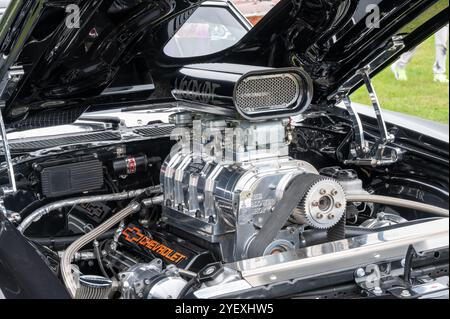 Un puissant moteur Chevrolet est mis en évidence lors d'un rassemblement de voitures classiques, avec un ventilateur poli et des détails chromés complexes, le tout en dessous Banque D'Images