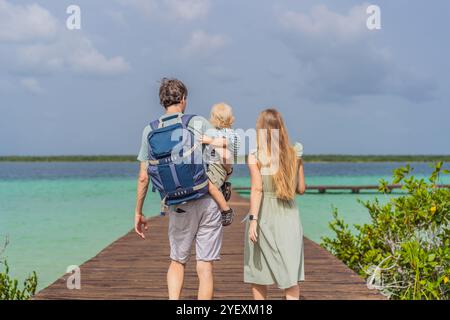 Maman, papa et leur bébé fils explorant la jetée en bois au-dessus des eaux turquoises du lac Bacalar, au Mexique. Concept de destination de voyage tropical paisible Banque D'Images