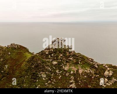 Vue aérienne d'une vallée entre des falaises couvertes de végétation, surplombant un vaste océan par temps nuageux Banque D'Images