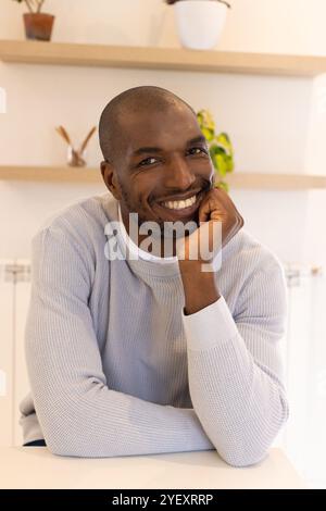 Homme afro-américain souriant dans un pull confortable assis à la maison, profitant d'un moment de détente Banque D'Images
