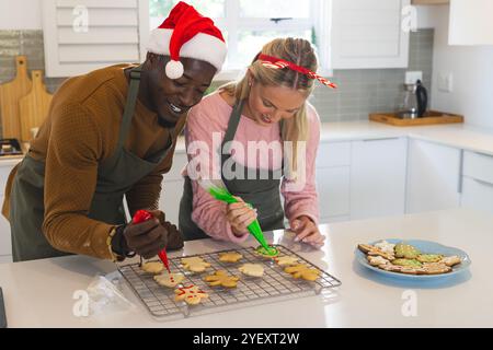 Décorer des biscuits de noël, couple multiracial heureux dans la cuisine festive, à la maison Banque D'Images