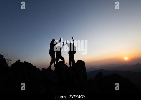 Silhouette d'ensemble surmontant les obstacles avec trois personnes tenant les mains en l'air sur le sommet de la montagne. concept d'entreprise de succès de travail d'équipe d'escalade Banque D'Images