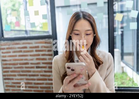 Heureuse jeune femme d'affaires mangeant du français frit tout en utilisant son téléphone à son bureau Banque D'Images
