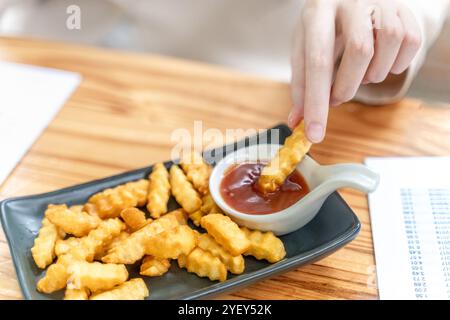 Gros plan sur la main d'une femme tenant une frite trempant dans du ketchup Banque D'Images