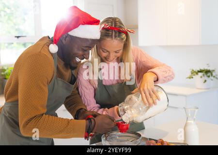 Noël, couple multiracial cuisiner ensemble, porter des vêtements de vacances festifs, à la maison Banque D'Images