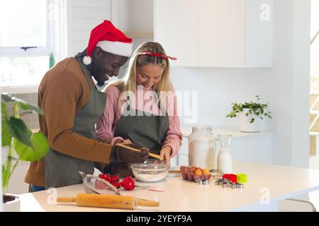 Noël, couple multiracial cuisson, port de vêtements de vacances festifs, à la maison Banque D'Images