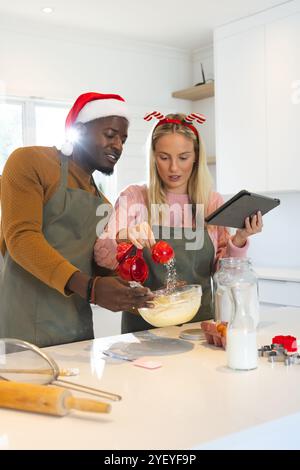 Temps de Noël, cuisson de couple multiracial , en utilisant la tablette pour les conseils de recette, à la maison Banque D'Images