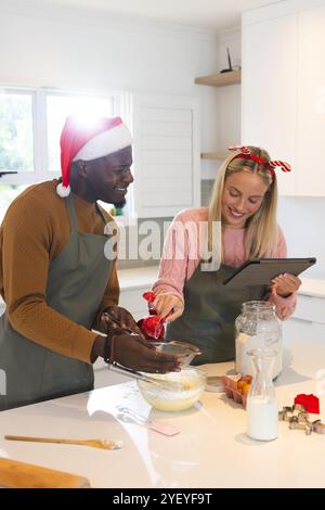 Temps de Noël, cuisson de couple multiracial , en utilisant la tablette pour la recette de vacances, à la maison Banque D'Images