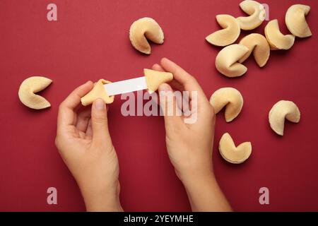 Femme tenant savoureux biscuit de fortune et papier avec prédiction sur fond rouge. Banque D'Images