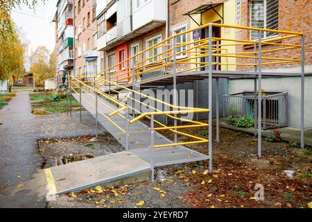 Une rampe nouvellement construite avec une rampe jaune vif mène à l'entrée du bâtiment résidentiel en briques. Une rampe près de la maison pour les personnes handicapées Banque D'Images