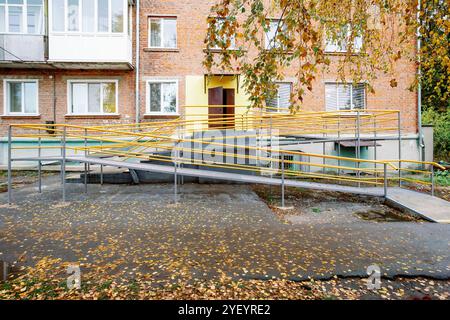 Une rampe nouvellement construite avec une rampe jaune vif mène à l'entrée du bâtiment résidentiel en briques. Une rampe près de la maison pour les personnes handicapées Banque D'Images