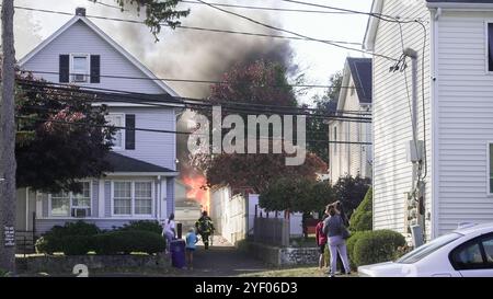 Une maison est en feu, et les gens regardent depuis la rue. Banque D'Images