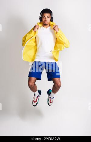 Homme, portrait et saut avec des écouteurs pour la musique, la mode ou le streaming audio sur un fond de studio gris. Jeune, homme ou modèle italien dans l'air Banque D'Images