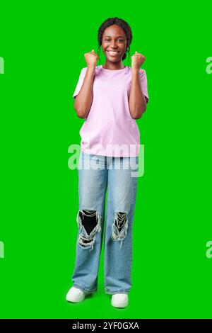 Une jeune femme avec des tresses exprime l'excitation avec un poing serré sur un fond vert vif Banque D'Images