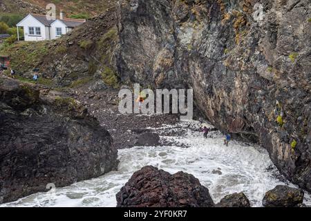 Les touristes à Kynance Cove sur la péninsule de Lizard se font prendre par de grandes vagues alors qu'ils tentent de traverser une plage rocheuse à Cornwall, Royaume-Uni, le 21 octobre 2024 Banque D'Images