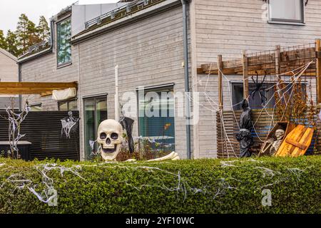 Affichage de cour d'Halloween avec crâne géant, squelette dans le cercueil, et toiles d'araignée contre fond de maison de banlieue moderne. Banque D'Images