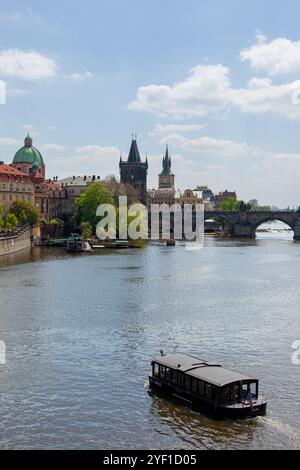 Un bateau-taxi traversant la rivière Vltava à Prague, avec le pont Charles et la tour du pont de la vieille ville à l'arrière - République tchèque. Banque D'Images