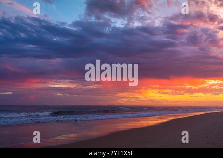 Les couleurs intenses du coucher de soleil de rouge, violet et orange remplissent le ciel et se reflètent sur le rivage. Banque D'Images