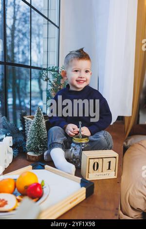 Un garçon de 2 ans est assis sur le rebord de la fenêtre le nouvel an. Ambiance du nouvel an à la maison. L'enfant attend la nouvelle année. Banque D'Images