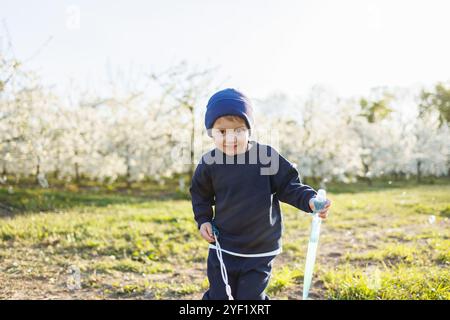 Un garçon de trois ans court dans un jardin fleuri avec des bulles de savon. Enfant joyeux et émotionnel marche dans le parc. Pains de savon pour enfants Banque D'Images