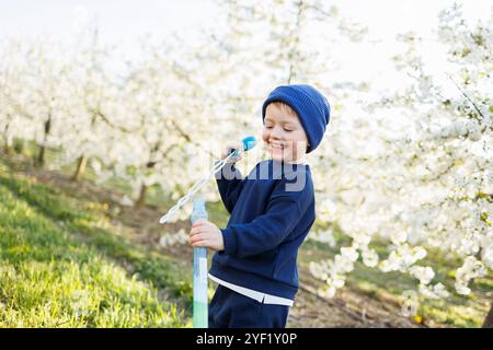 Un garçon de trois ans court dans un jardin fleuri avec des bulles de savon. Enfant joyeux et émotionnel marche dans le parc. Pains de savon pour enfants Banque D'Images