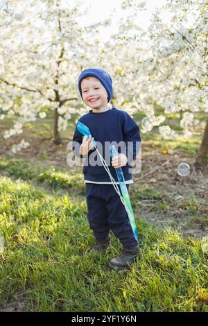 Un garçon de trois ans court dans un jardin fleuri avec des bulles de savon. Enfant joyeux et émotionnel marche dans le parc. Pains de savon pour enfants Banque D'Images