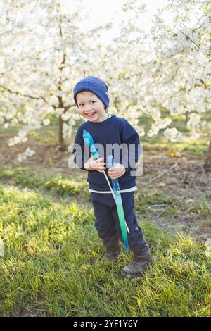 Un garçon de trois ans court dans un jardin fleuri avec des bulles de savon. Enfant joyeux et émotionnel marche dans le parc. Pains de savon pour enfants Banque D'Images