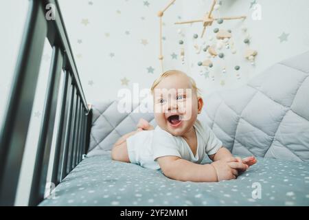 Photo d'un bébé de 5 mois allongé dans un berceau. Un lit bébé avec un petit garçon dans un body blanc. Banque D'Images