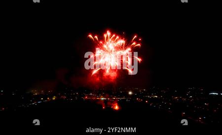 Un feu d'artifice rouge explose dans le ciel nocturne. Une ligne d'horizon de la ville avec des lumières est visible ci-dessous. Banque D'Images