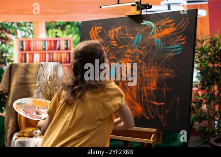 Dans un atelier créatif, une artiste féminine mélange des pigments avec ses doigts pour obtenir la teinte parfaite. La création est un chef-d'œuvre abstrait reflétant son talent de peinture au doigt et son inspiration. Banque D'Images