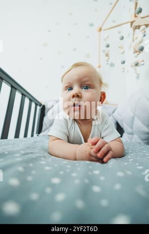 Photo d'un bébé de 5 mois allongé dans un berceau. Un lit bébé avec un petit garçon dans un body blanc. Banque D'Images