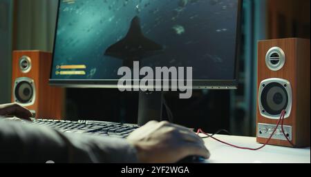 Joueur utilisant le clavier et la souris filaire pour jouer à des jeux vidéo sur PC de bureau, gros plan. Homme jouant au jeu en ligne devant le moniteur avec des périphériques informatiques au bureau dans l'appartement, caméra B. Banque D'Images