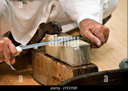 Homme aiguisant une épée japonaise courte appelée wakizashi de manière traditionnelle avec une pierre à aiguiser dans la ville de Seki, Gifu, Japon. Banque D'Images