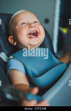 Un garçon de 1 an est assis dans une chaise haute et mange du pain. Le bébé mange du pain. L'auto-alimentation de l'enfant. Banque D'Images