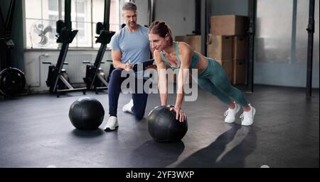 Entraîneur personnel montrant l'entraînement sportif push-up dans le gymnase avec balle. Fitness féminin Banque D'Images