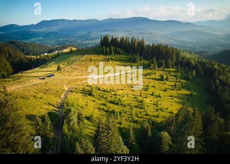 Vue aérienne à couper le souffle du paysage de montagne au coucher du soleil. La lumière dorée baigne les collines ondoyantes et les forêts luxuriantes, créant une scène sereine et idyllique. Montagnes lointaines ajoutant de la profondeur à la vue pittoresque. Banque D'Images