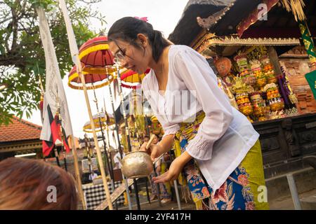 Une travailleuse hindoue balinaise arrosant de l'eau sur les visiteurs, cérémonie Kuningan, Temple Pura Gunung Sari, Denpasar, Bali, Indonésie, Asie Banque D'Images