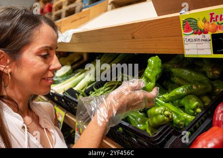 Une femme achète des légumes dans une épicerie. Elle porte des gants et tient un poivre Banque D'Images