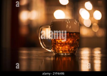 Une tasse en verre débordant de bière tchèque dorée est en évidence dans cette photographie de nuit. Le fond est orné de motifs lumineux circulaires, Banque D'Images