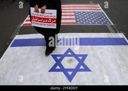 Téhéran, Iran. 3 novembre 2024. Les gens marchent sur les drapeaux américains et isréaux lors d'un rassemblement anti-américain marquant le 45e anniversaire de la prise de contrôle de l'ambassade américaine devant l'ancien bâtiment de l'ambassade à Téhéran. Le 4 novembre 1979, des étudiants iraniens se sont emparés de l'ambassade des États-Unis à Téhéran, retenant en otage plus de 50 diplomates et gardes américains pendant 444 jours. Crédit : ZUMA Press, Inc Crédit : ZUMA Press, Inc/Alamy Live News Banque D'Images