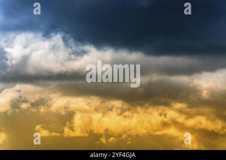 Bleu dramatique nuages orageux sur le dessus et jaune-golden fluffy clouds éclairée par des rayons de soleil sur ci-dessous. Vue imprenable sur la météorologie naturelles arrière-plan. Banque D'Images