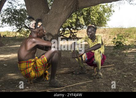 Deux jeunes hommes avec des coiffes traditionnelles en argile assis sur des appuie-têtes en bois convertis en tabourets, groupe ethnique Dassanetsch, sud de la vallée de l'Omo, Ethi Banque D'Images