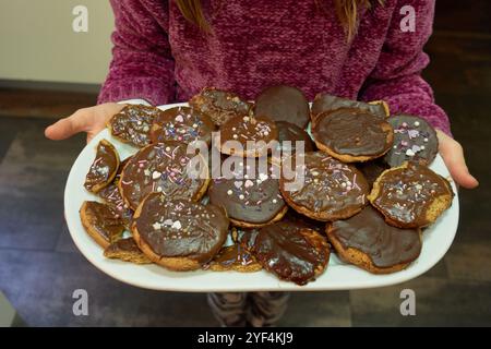 Enfant tenant avec ses mains un plateau blanc rempli de biscuits recouverts de chocolat maison décorés de saupoudres Banque D'Images