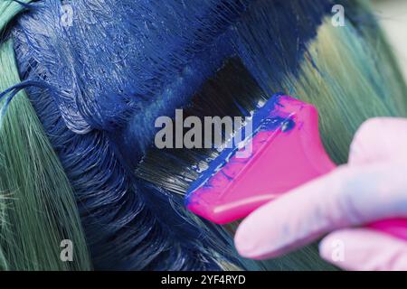 Gros plan sur la coloration des cheveux au salon de beauté. Coiffeur à l'aide d'une brosse rose tout en appliquant de la peinture bleue à la femme pendant le processus de teinture des cheveux en co unique Banque D'Images